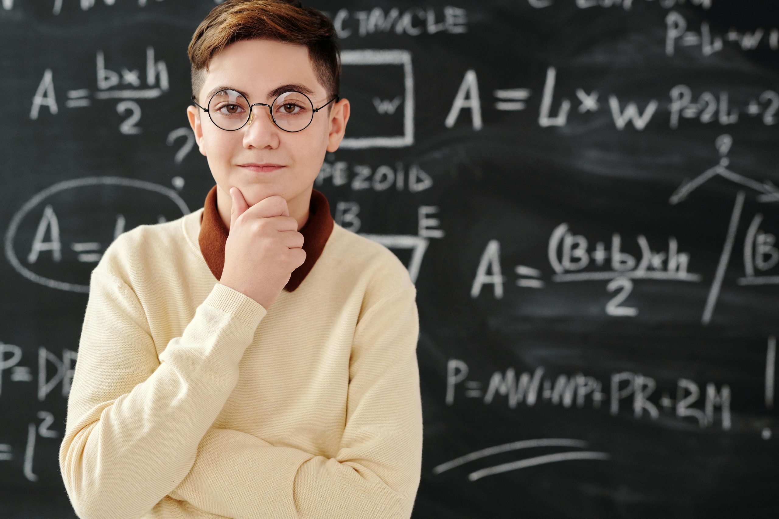 Smart student in glasses posing confidently in front of a blackboard full of mathematical equations.